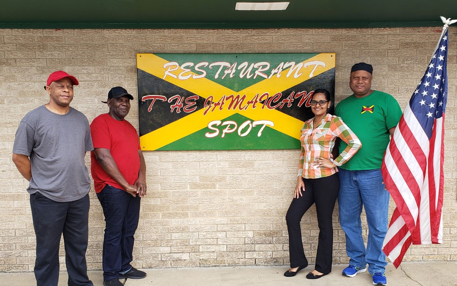 Restaurant owners stand in front of the Jamaican Spot sign